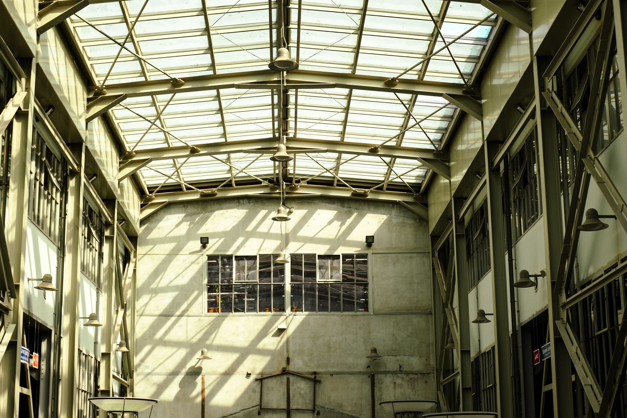 Una nave industrial con el techo de cristal: la luz entra a franjas por las vigas de hierro y cae sobre la pared del fondo