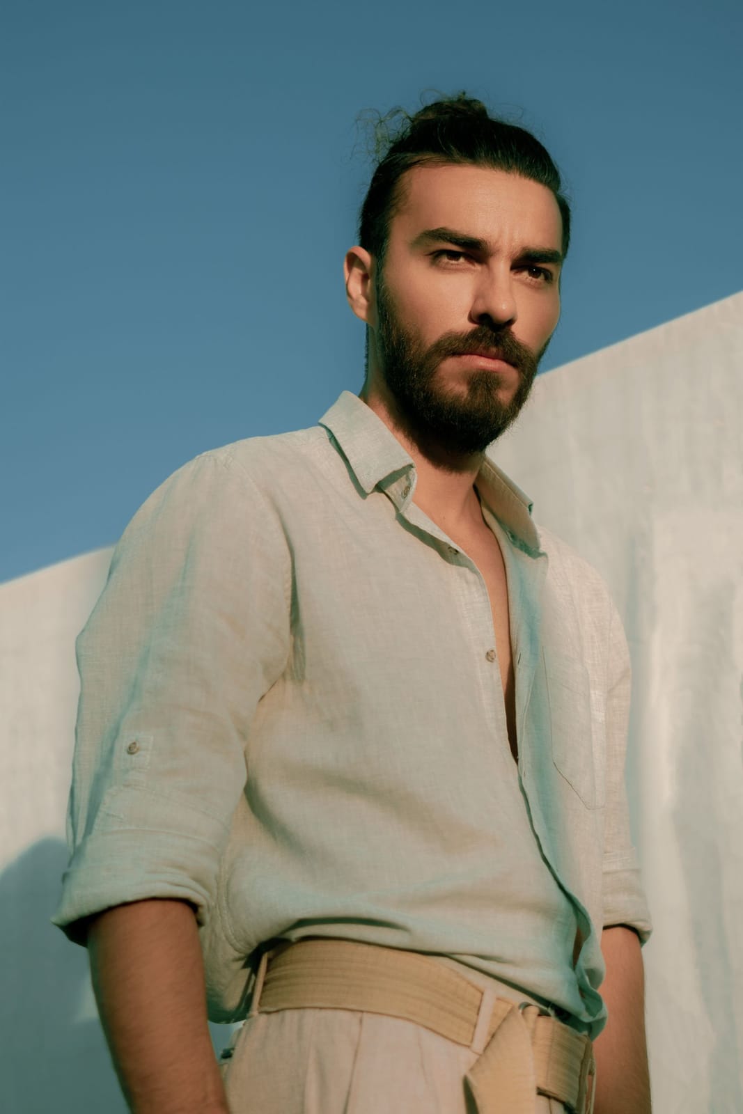 Desde abajo, la camisa de lino abierta en el cuello contra el cielo y una pared blanca