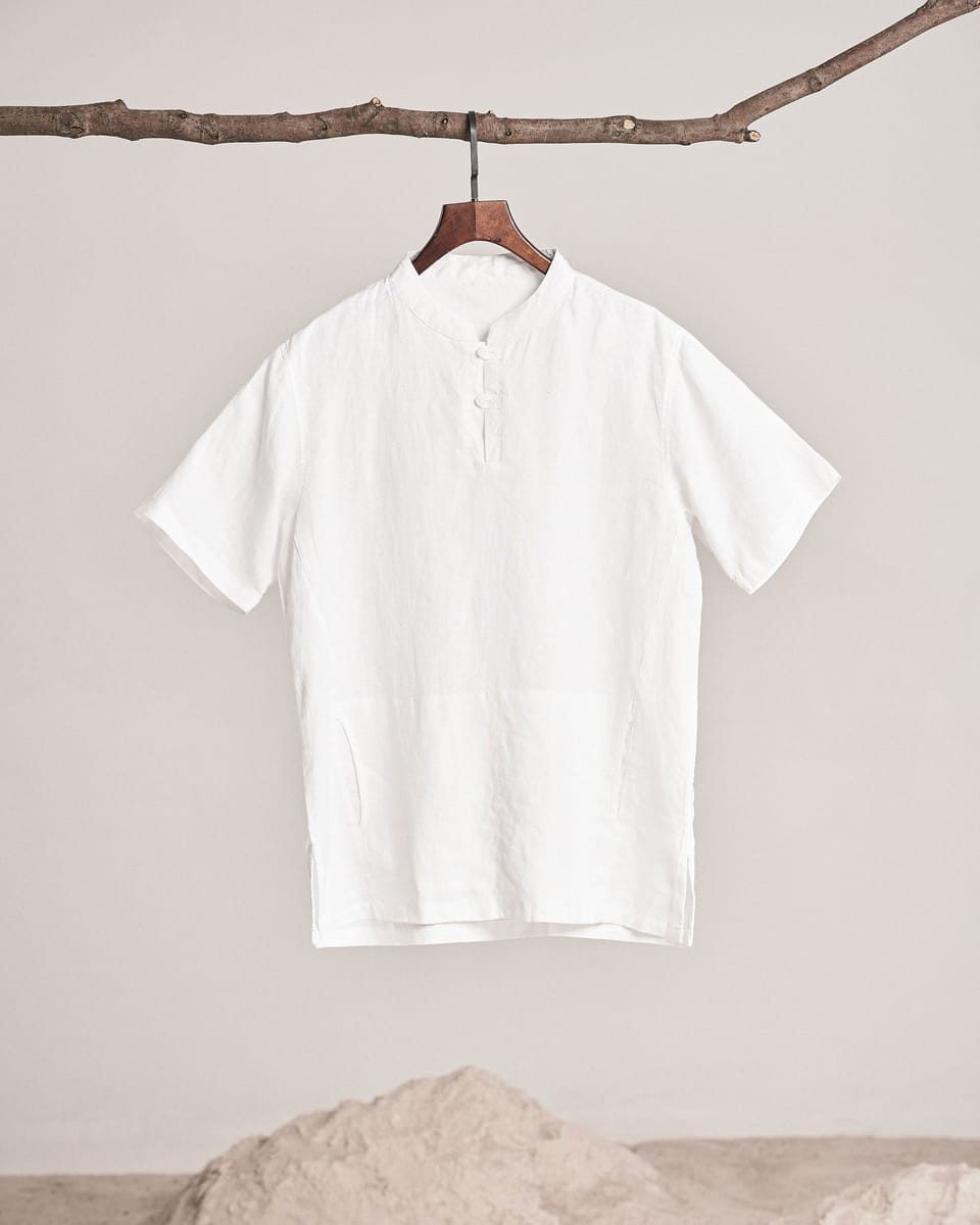 La camisa Garbí de lino blanco, manga corta y cuello mao, colgada de una rama